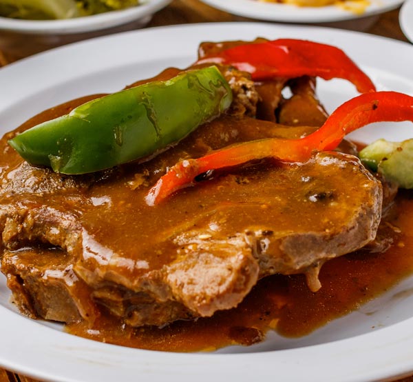 Indulge in our smothered pork chops, featuring juicy chops cooked to perfection and smothered in a rich, savory gravy for a comforting meal.